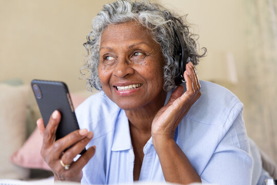 Smiling african american senior woman listening music and using smartphone while lying on bed