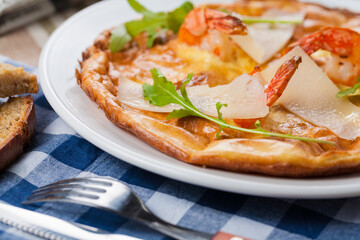 Italian pizza with shrimps, arugula, parmesan on a white plate and checkered tablecloth