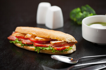 sandwich with ham and tomato on a black background with a cream soup