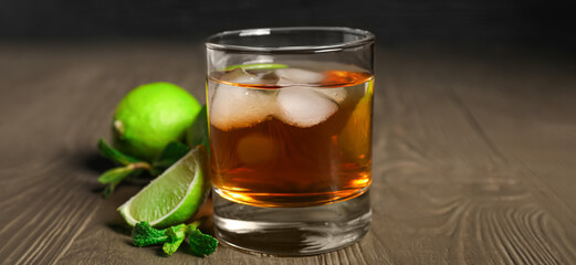 Glass of rum with ice and lime on wooden table