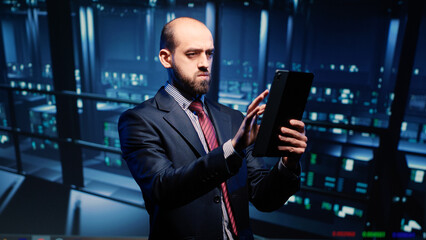 Fototapeta premium Datacenter engineer looking at mainframe diagnostics using digital tablet, inspecting cloud computing server room. IT infrastructure specialist working with fintech in data center.