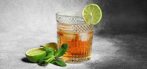 Glass of rum with ice, mint and lime on grey background