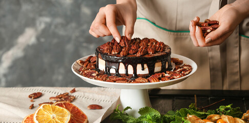 Female confectioner decorating tasty chocolate cake at table, closeup