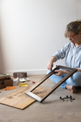 woman with carpenter's tools, performs work with wooden furniture, sitting on the floor at home
