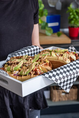 A man in black clothes holds a white tray with toasted avocado buns. The tacos on a large white and gray napkin. Gray background