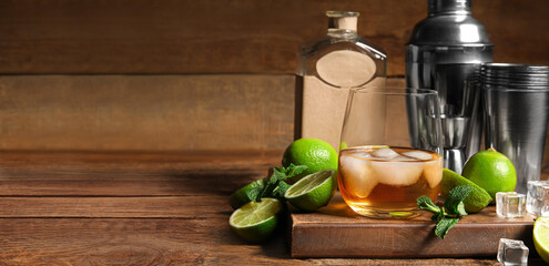 Glass of rum, bottle, shaker, mint and lime on wooden background with space for text
