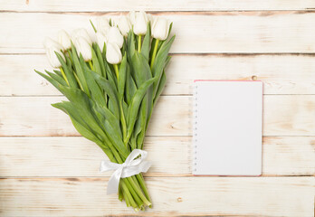 White tulip bouquet with notebook on wooden background, top view