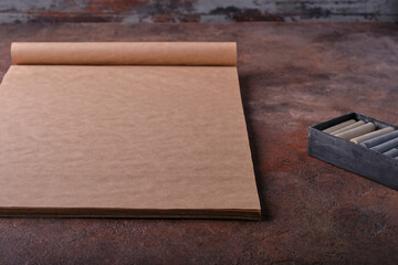 Close-up of a large beautiful art album with textured sheets of craft paper and a box with gray Pastel crayons for drawing. The concept of the artist's working corner, materials and tools for drawing