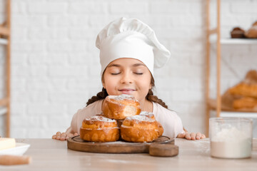 Little baker and tasty buns on table in kitchen, closeup