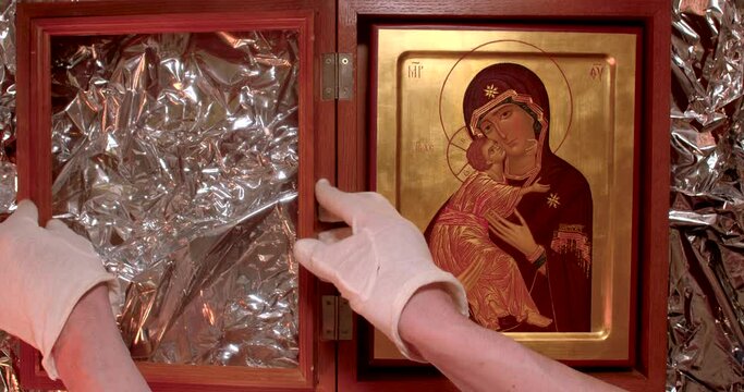 The hands of a museum worker hold Christian icon depicting the Virgin Mary with a baby in their hands. A symbol of the Church, symbolize purity, virginity, love, royalty, innocence, everlasting life.