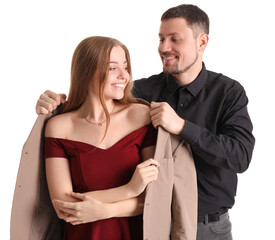 Young man putting jacket onto his wife on white background