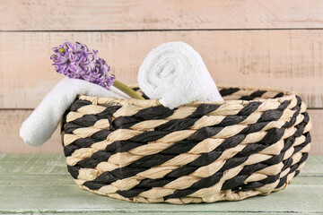 Fototapeta na wymiar Basket with rolled soft towels and hyacinth flower on green wooden table