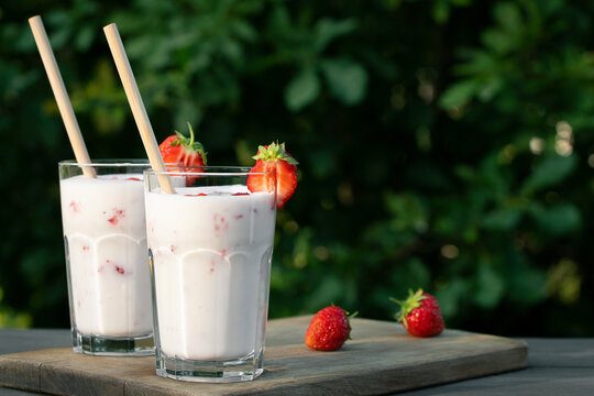 Strawberry smoothie in two glass glasses and fresh strawberries on a wooden table in the yard, copyspace