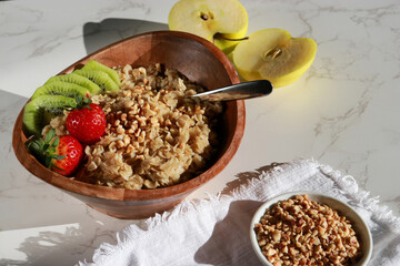 close up of healthy homemade oatmeal in a wooden bowl with fruits on white table