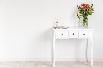 Vases with beautiful alstroemeria flowers, magazines and reed diffuser on table near light wall