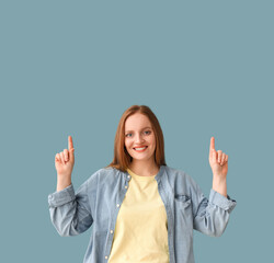 Beautiful redhead woman pointing at something on blue background