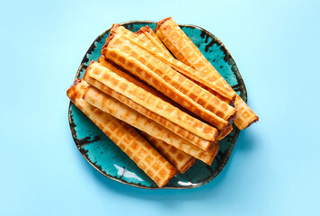 Plate of wafer rolls with boiled condensed milk on blue background