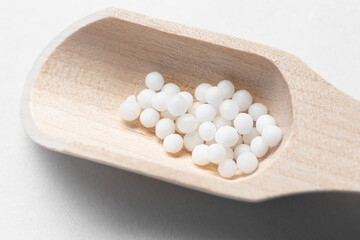 Fototapeta na wymiar White homeopathic granules on a small wooden scoop