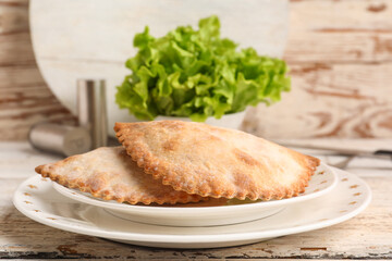 Plate with baked meat empanadas and lettuce on light wooden table, closeup