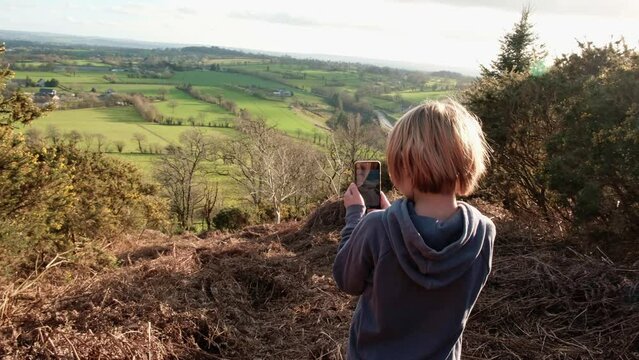 A boy takes a picture of a natural view from a mountain on a mobile phone. Hiking, photographed with a beautiful view. School holidays, travel.