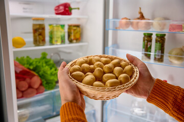 male hands put a basket of organic potatoes in the fridge