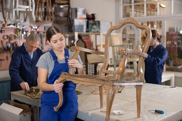 Young female carpenter working on making vintage chair in workshop