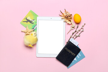 Tablet computer with seashells, passport, willow branches, chicken and Easter egg on pink background