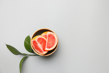 Bowl with pieces of ripe grapefruit and plant branch on light background