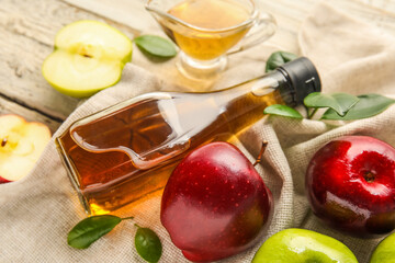Glass bottle of fresh apple cider vinegar and fruits on white wooden background