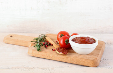 Board with bowl and spoon of tasty tomato paste on white wooden background