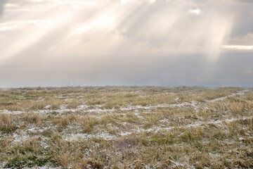 A grassy hill with early winter snow, rays of light from sunlight and mist in background, nobody