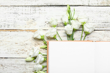Composition with blank open book and beautiful eustoma flowers on light wooden background, closeup
