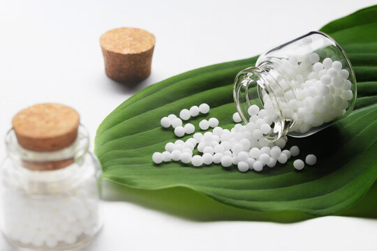 Homeopathic pills scattered from a bottle on a green leaf