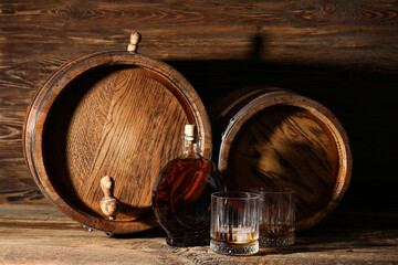 Oak barrels with bottle and glasses of cold whiskey on wooden background