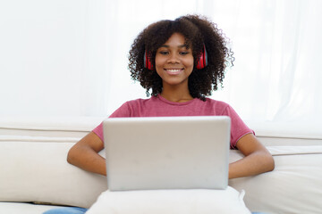 Fototapeta na wymiar American - African black young woman sitting on sofa in living room and enjoy watching a social media on laptop computer in free time.