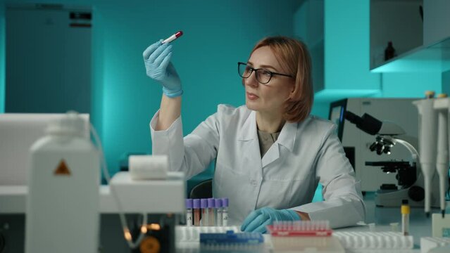 A doctor in glasses and lab coat incpecting a test tube with dark red blood. She is a scientific expert performing an important sample analysis. High quality 4k footage 