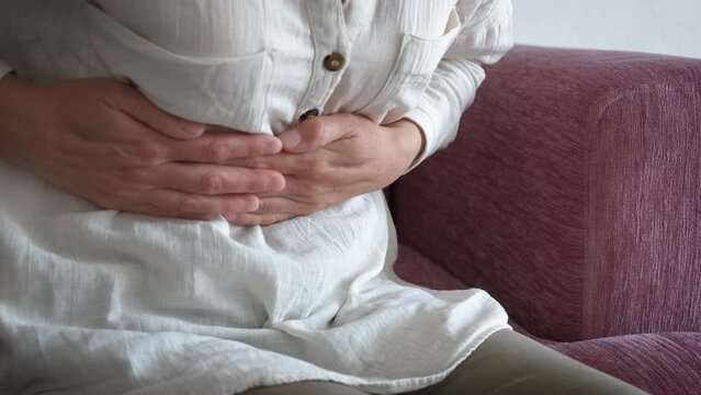 Lady massaging painful belly indoor. A woman with health problems massaging her belly because of pain. A concept of menstruation spasms or health problems.