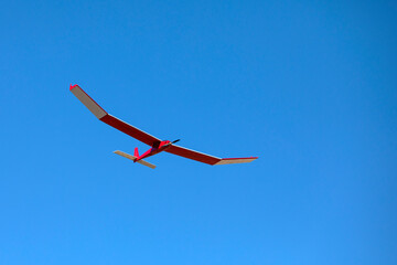 A radio controlled powered model glider soars against a blue sky background.