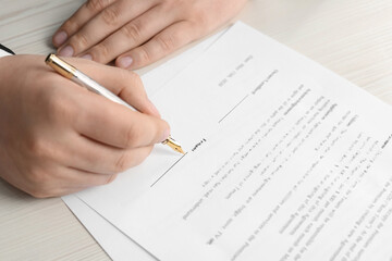 Notary signing document at wooden table, closeup