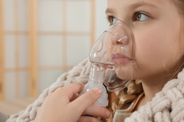 Little girl using nebulizer for inhalation at home, closeup