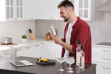 Man learning to make cocktail with online video on laptop at table in kitchen. Time for hobby