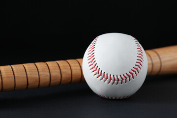 Wooden baseball bat and ball on black background, closeup. Sports equipment