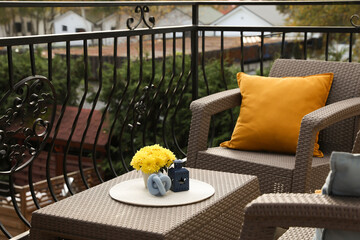 Orange pillow and yellow chrysanthemum flowers on rattan garden furniture outdoors