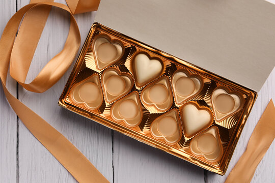 Partially empty box of chocolate candies on white wooden table, top view