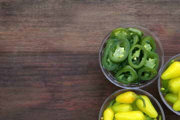 Pickled green and yellow jalapeno peppers on wooden table, flat lay. Space for text