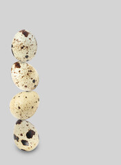 Stacked speckled quail eggs on light grey background. Space for text