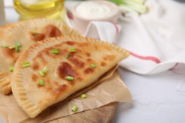 Delicious fried chebureki with cheese and green onion on white textured table, space for text