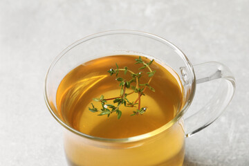 Glass cup of aromatic herbal tea with thyme on light grey table, closeup