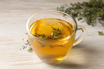 Cup of fresh thyme tea on wooden table, closeup