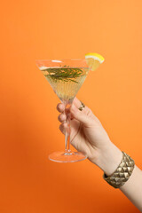 Woman holding martini glass of refreshing cocktail with lemon slice and rosemary on orange...